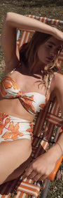 Model wearing a Green & Orange Twist Bikini Top while lounging on a beach chair.