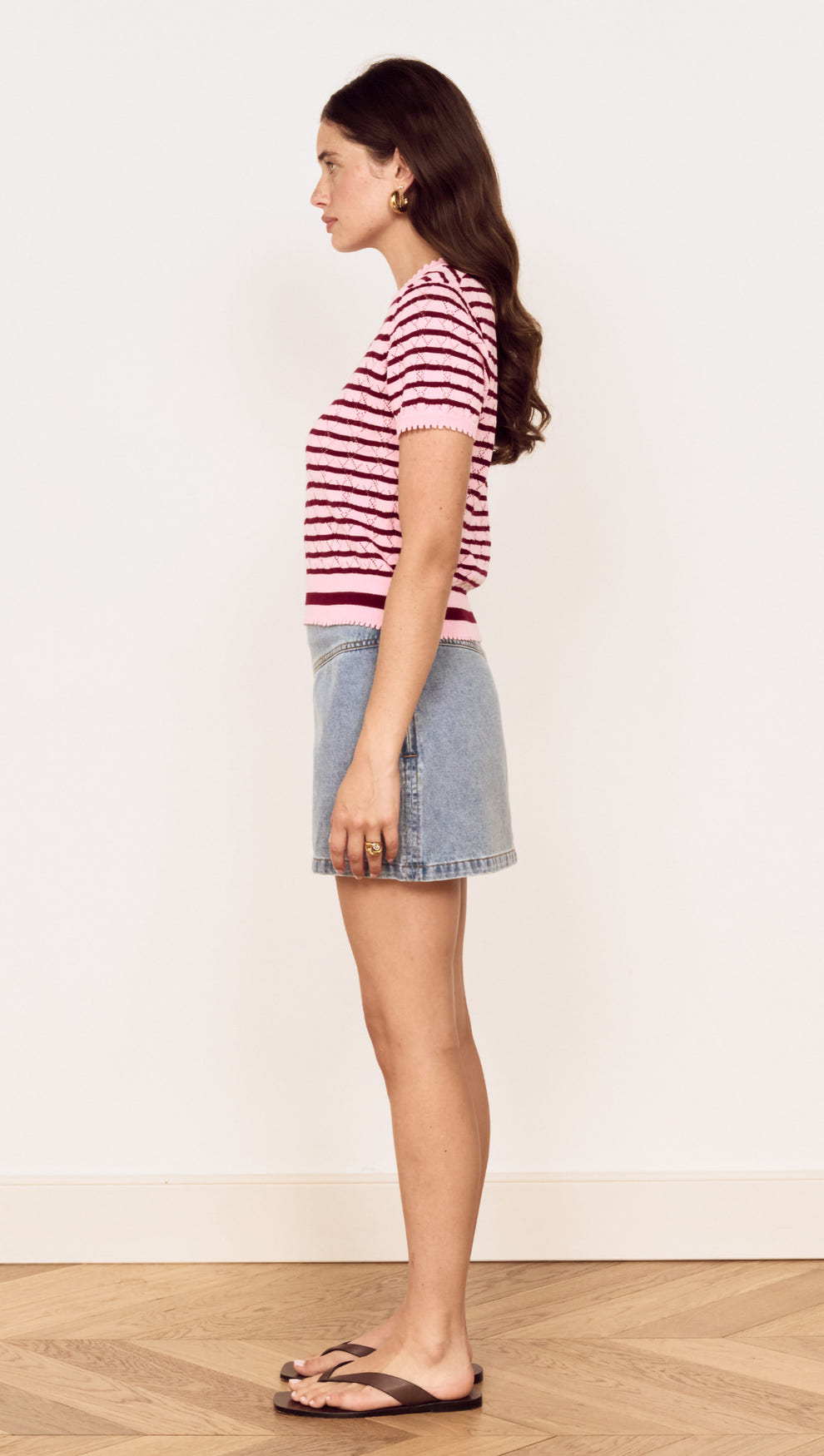 Model showcasing the Pink Stripe Pointelle Knit Tee in pink and burgundy stripes paired with a denim skirt.
