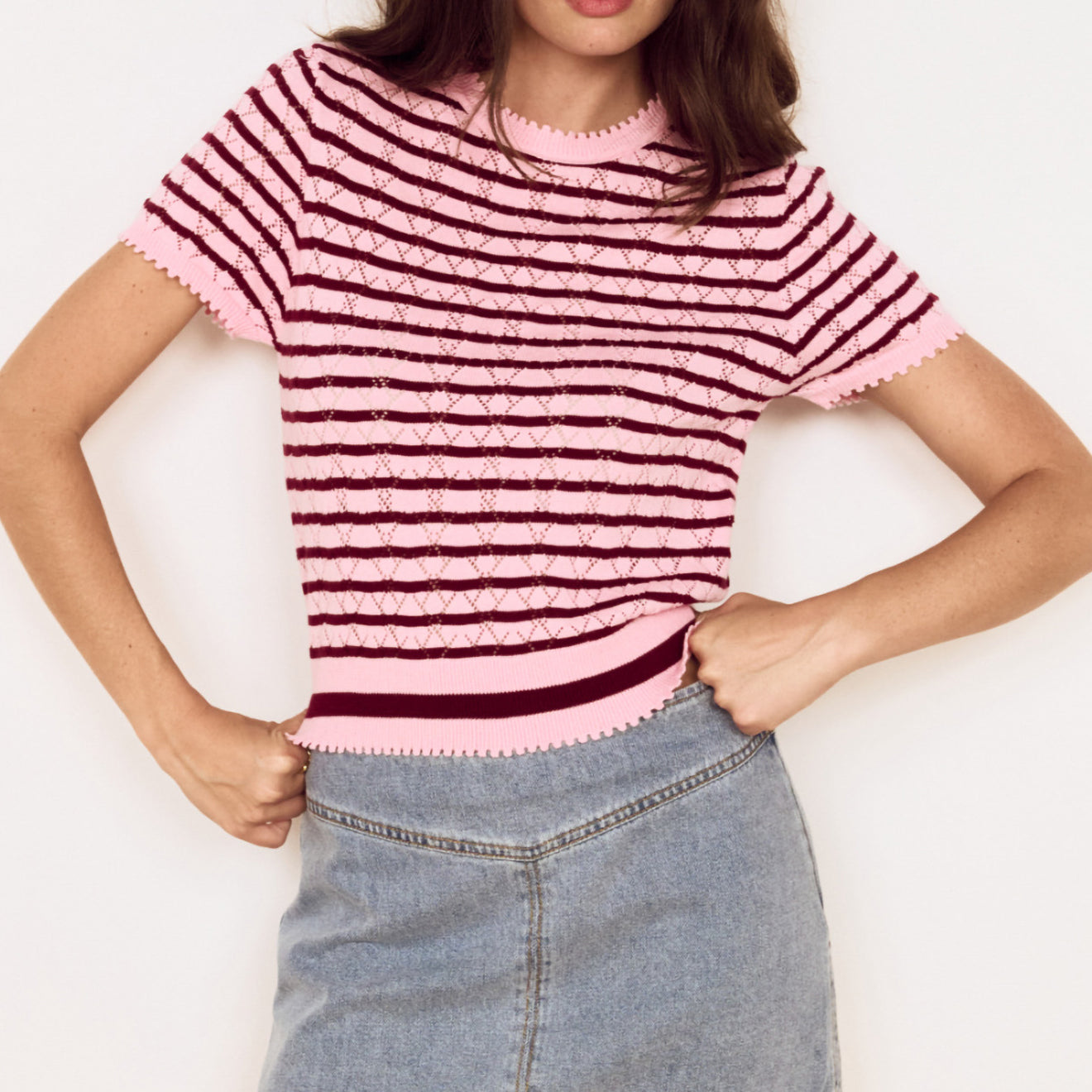 Model wearing a Pink Stripe Pointelle Knit Tee with openwork knit and horizontal stripes, styled with a denim skirt.