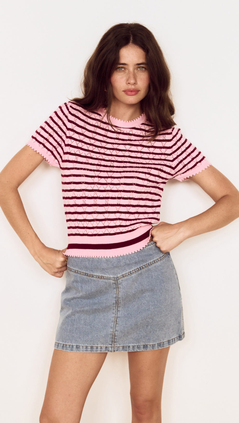 Model wearing a Pink Stripe Pointelle Knit Tee with openwork knit and horizontal stripes, styled with a denim skirt.