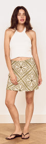Model wearing Scarf Print Bias Mini Skirt in Olive with a white halter top, showcasing a floral print.