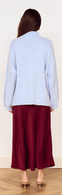 Back view of a model wearing a light blue sweater and a Burgundy Side Split Bias Midi Skirt on a wooden floor.