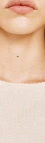 Close-up of a model's neckline wearing a Boat Neck Rib Detail Mesh Top in Cream, showcasing textured fabric and subtle details.