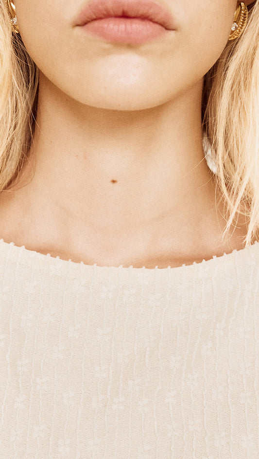 Close-up of a model's neckline wearing a Boat Neck Rib Detail Mesh Top in Cream, showcasing textured fabric and subtle details.
