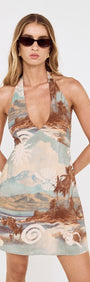 Model wearing the Island Print Halterneck Mini Dress featuring a scenic seaside print and a plunging neckline.