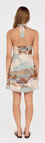 Back view of a model wearing the Island Print Halterneck Mini Dress, showcasing scenic print and A-line mini skirt.