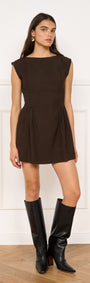 Pleat Waisted Mini Dress in Chocolate modeled with a boat neckline and gathered skirt, paired with knee-high black boots.