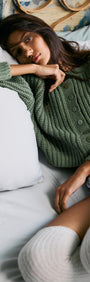 Model lounging in bed wearing a Green Cable Knit Cropped Cardigan with ribbed texture and button-front closure.