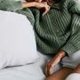 Model lounging in bed wearing a Green Cable Knit Cropped Cardigan with ribbed texture and button-front closure.