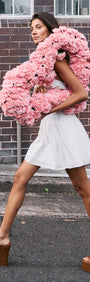 Model wearing a White Cotton Broderie Mini Dress, holding a pink floral accessory while walking on the street.