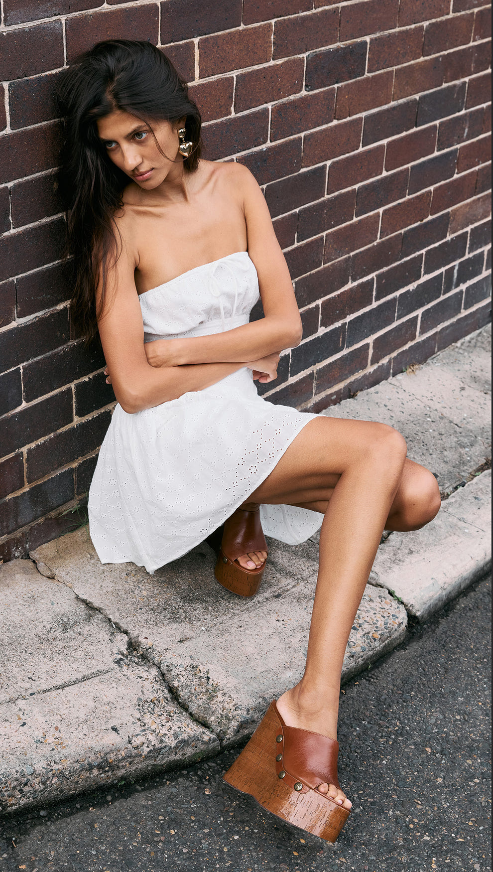 Model wearing a White Cotton Broderie Mini Dress, featuring a strapless design and a flared skirt, paired with brown platform shoes.