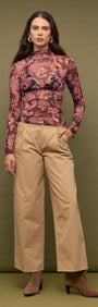 Model wearing a Sheer Printed Long Sleeve Mesh Top with patterned fabric and high neckline, styled with wide-leg pants.