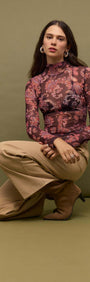 Model wearing Sheer Printed Long Sleeve Mesh Top with fitted silhouette on green background.