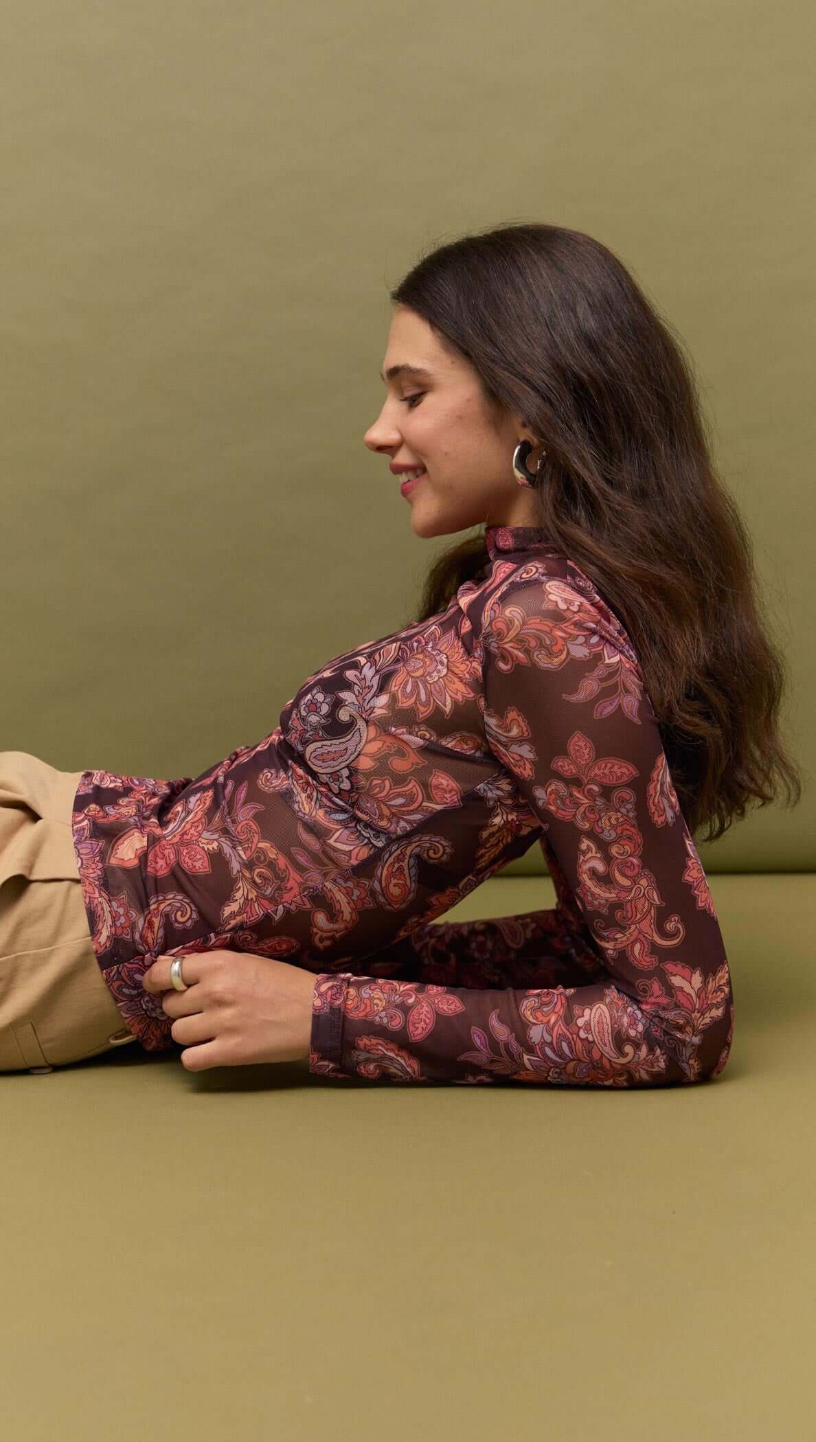 Model wearing Sheer Printed Long Sleeve Mesh Top in a floral print, styled on a green background.