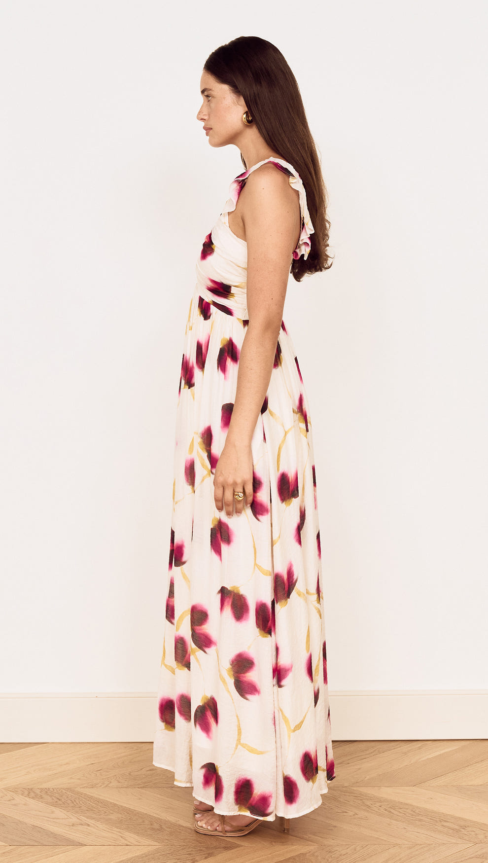 Model wearing a Floral Ruffle Detail Bias Maxi Dress showcasing a side view with a floral design in berry and gold tones.