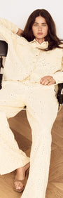 Model wearing a Cotton Denim Broderie Anglaise Jacket paired with matching bottoms, sitting on a chair.