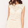 Woman wearing Cream Cotton Lace Micro Tee with floral lace detail and cap sleeves, styled for elegant occasion wear.