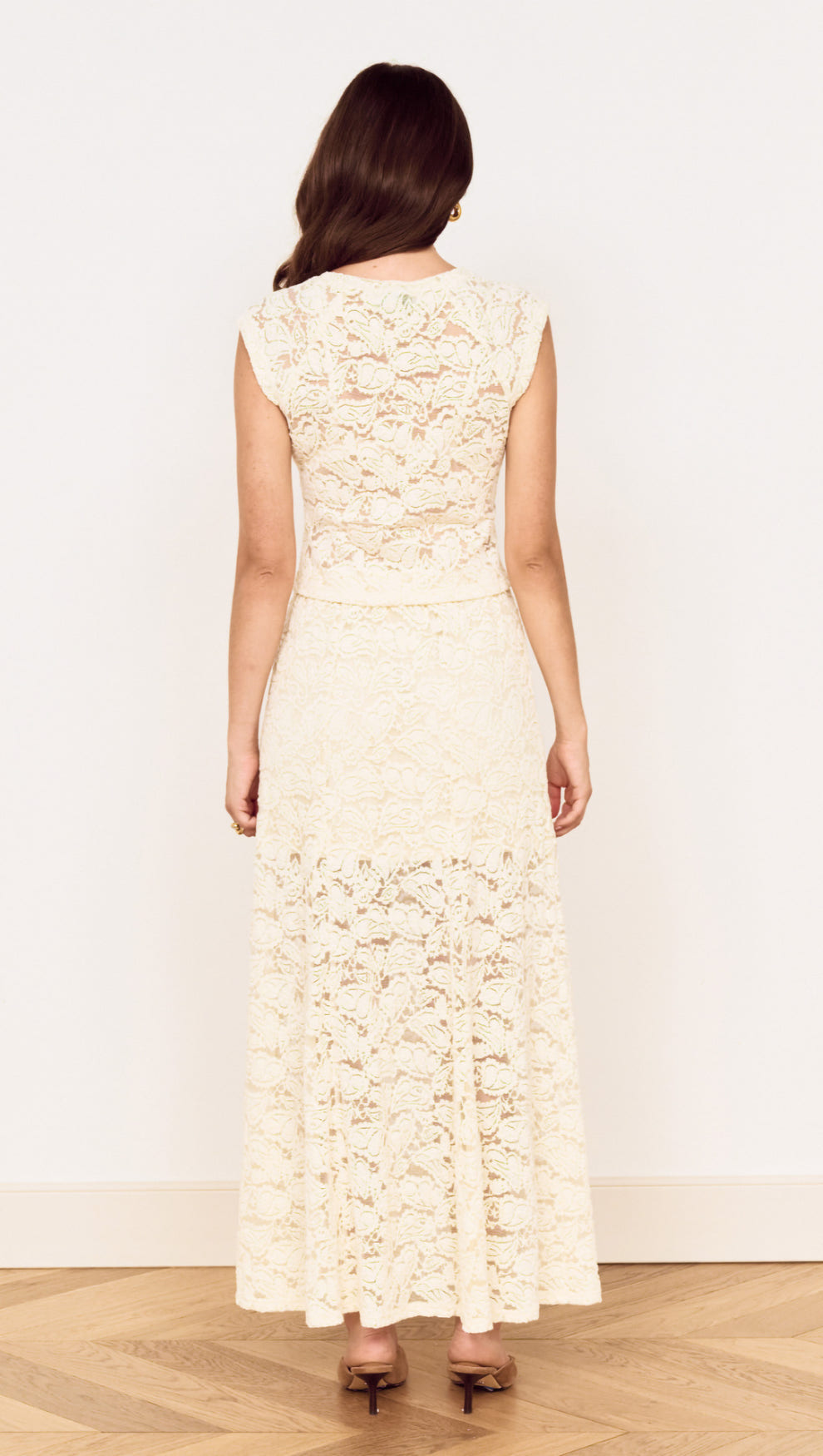 Back view of a woman wearing a Cream Cotton Lace Maxi Skirt with floral lace detailing and a flowing silhouette.