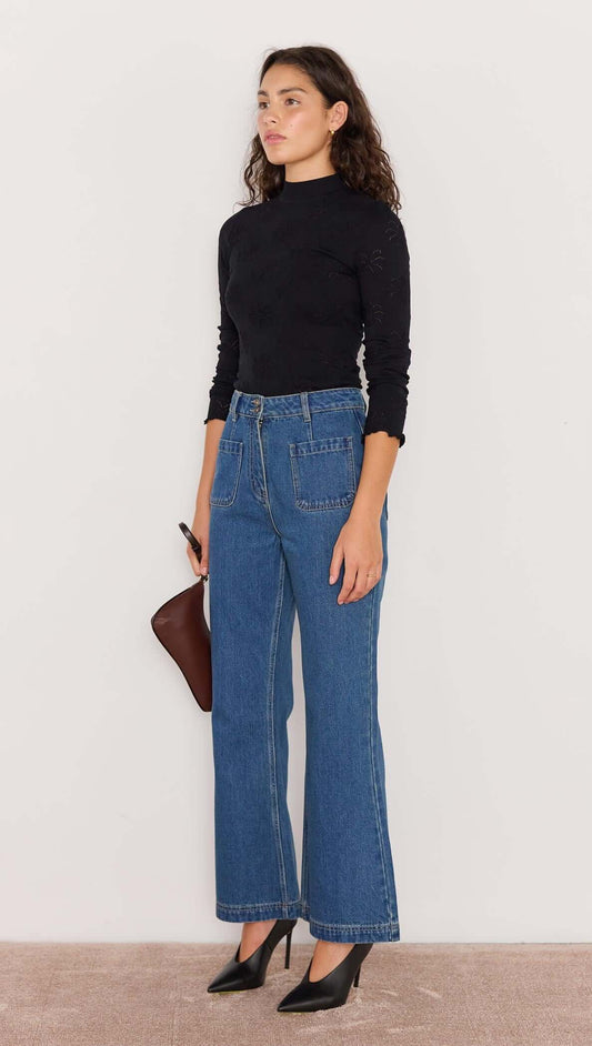 Model wearing high-waisted Nora Bootcut Jeans in vintage blue, styled with a black top and heels.