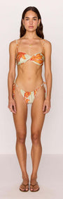 Model wearing a Green & Orange Twist Bikini Top with sunset floral print, showcasing twisted front detail and beaded straps.