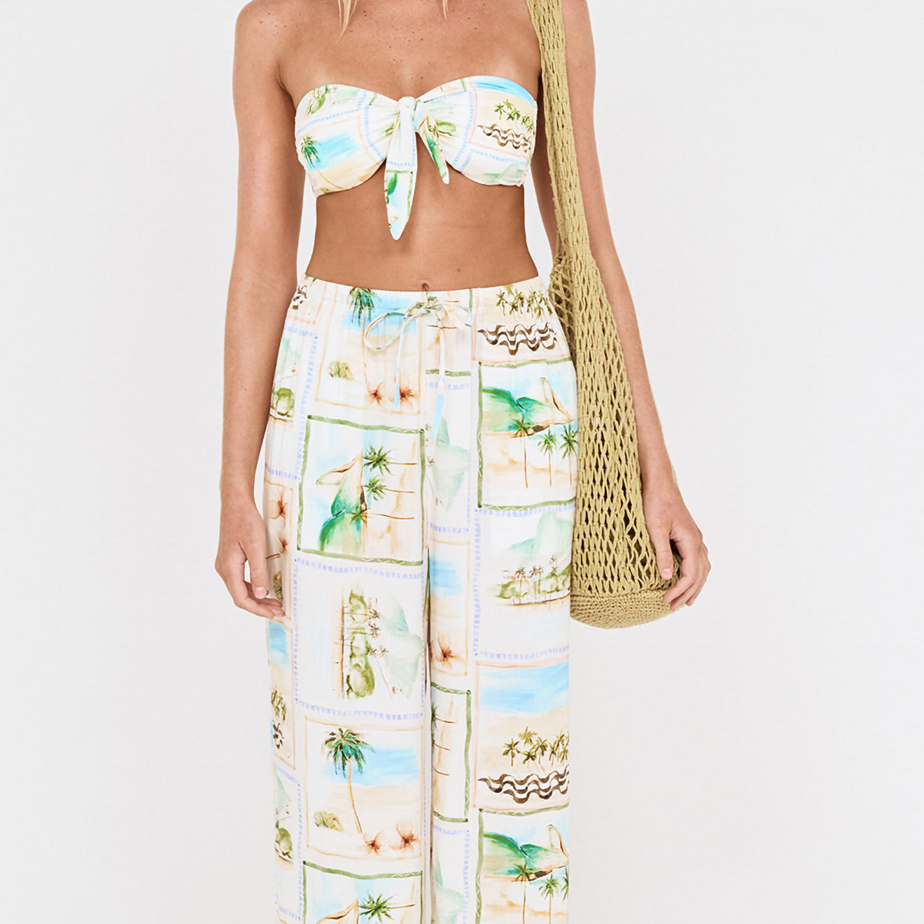 Woman wearing Island Postcard Knot Front Strapless Bikini Top with postcard-print pants and a bag.