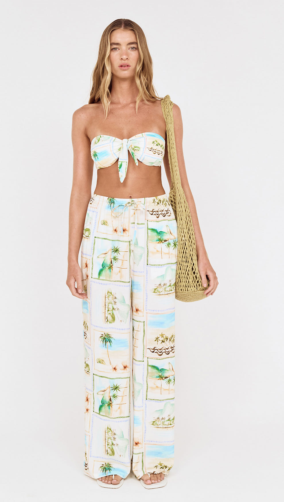 Woman wearing Island Postcard Knot Front Strapless Bikini Top with postcard-print pants and a bag.