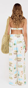 Model wearing Island Postcard Drawstring Beach Pants and a bikini top, holding a patterned tote bag, showcasing a tropical look.