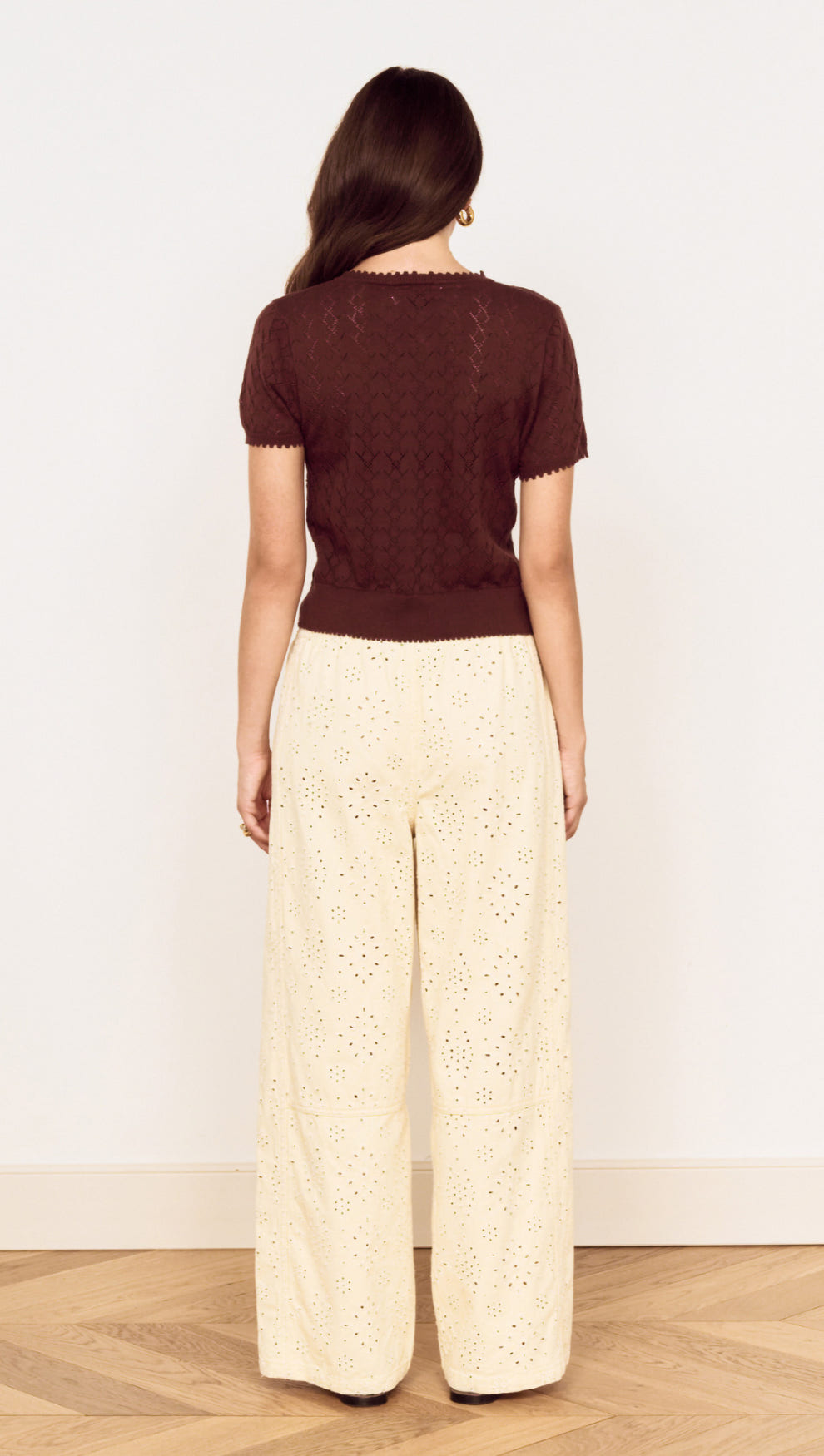 Back view of a model wearing a Brown Scallop Edge Knitted Tee with wide-leg eyelet trousers.