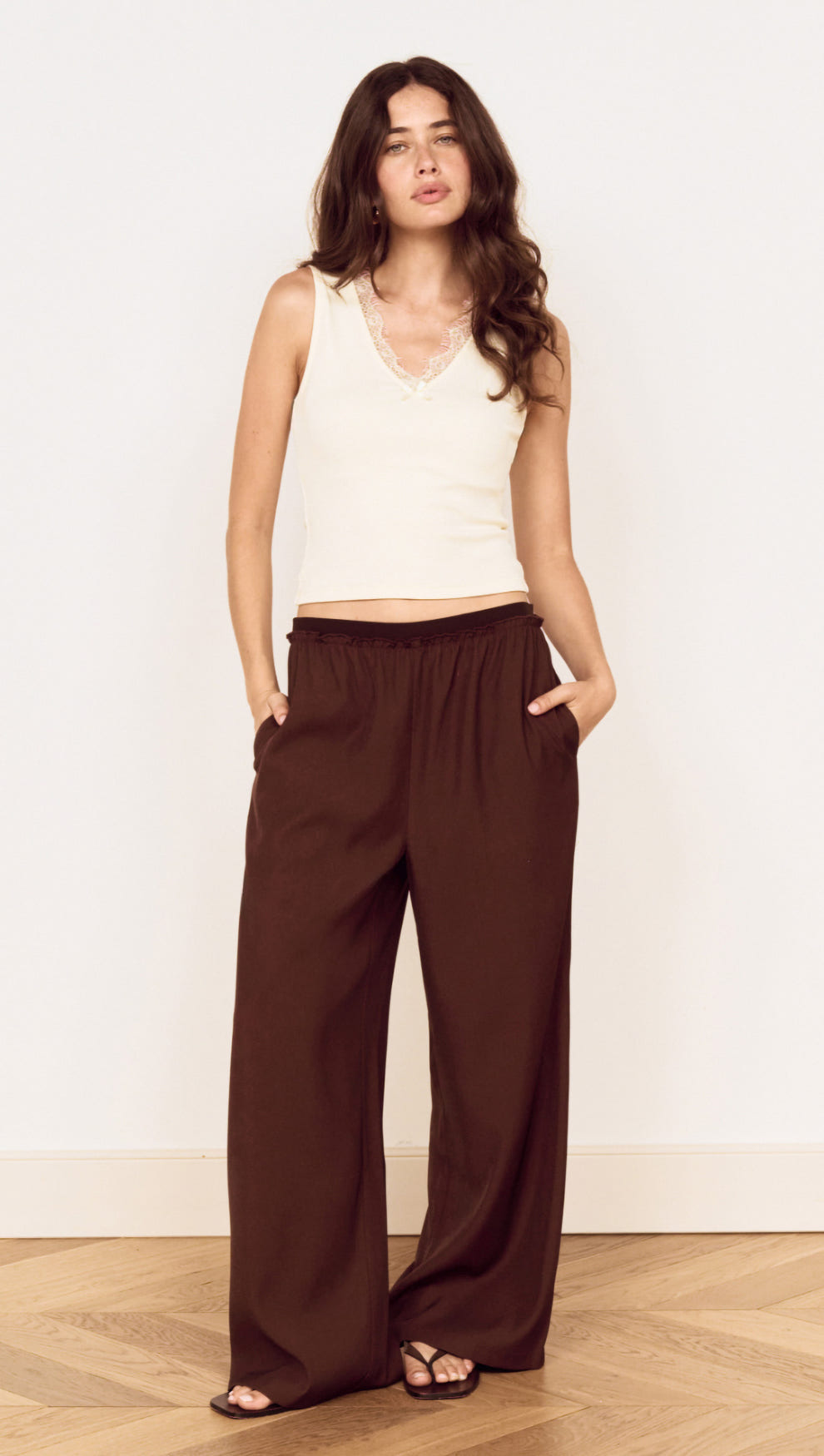 Model wearing a Cream Cotton Blend Tank with Lace Trim paired with relaxed brown pants, showcasing a stylish everyday outfit.