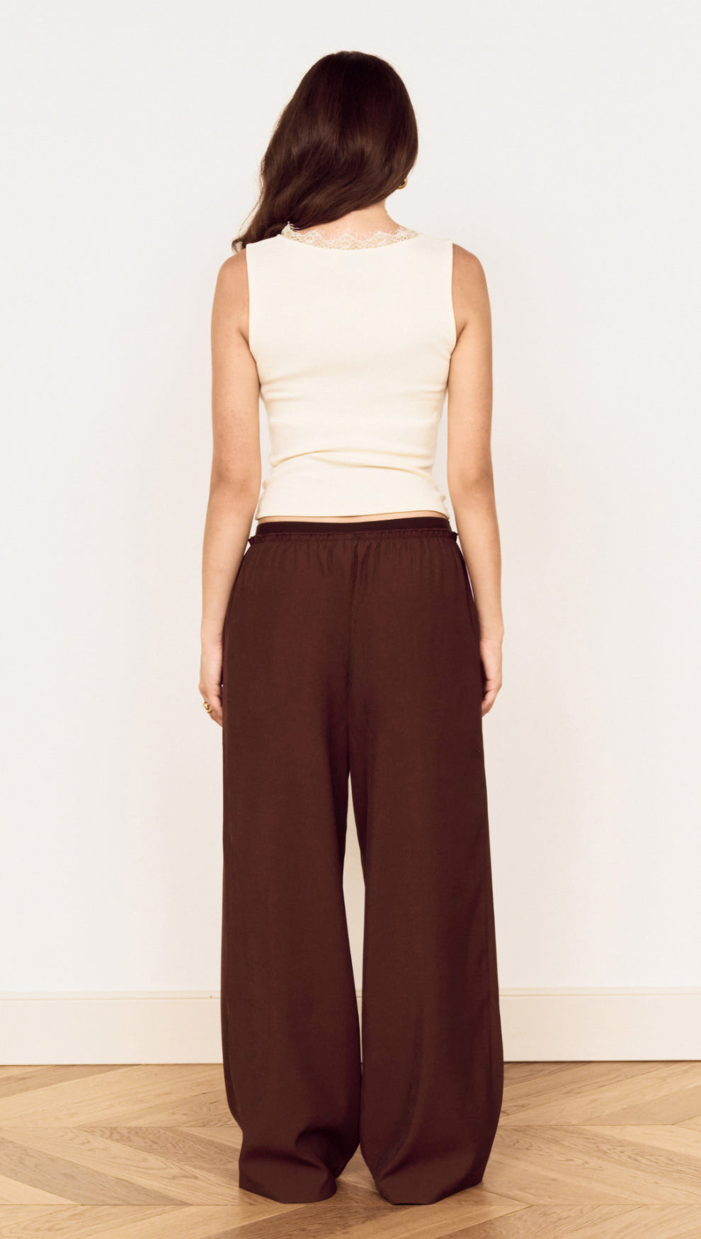 Back view of a woman wearing a Cream Cotton Blend Tank with Lace Trim and brown wide-leg pants.