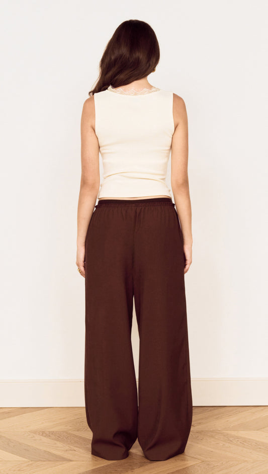 Back view of a woman wearing a Cream Cotton Blend Tank with Lace Trim and brown wide-leg pants.