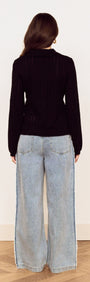 Back view of a woman wearing a Black Scallop Edge Pointelle Cardigan with wide-leg jeans.