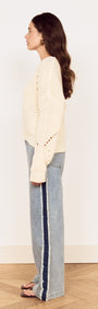 Side view of a model wearing a Cream Round Neck Open Knit Jumper with relaxed fit denim for a casual look.
