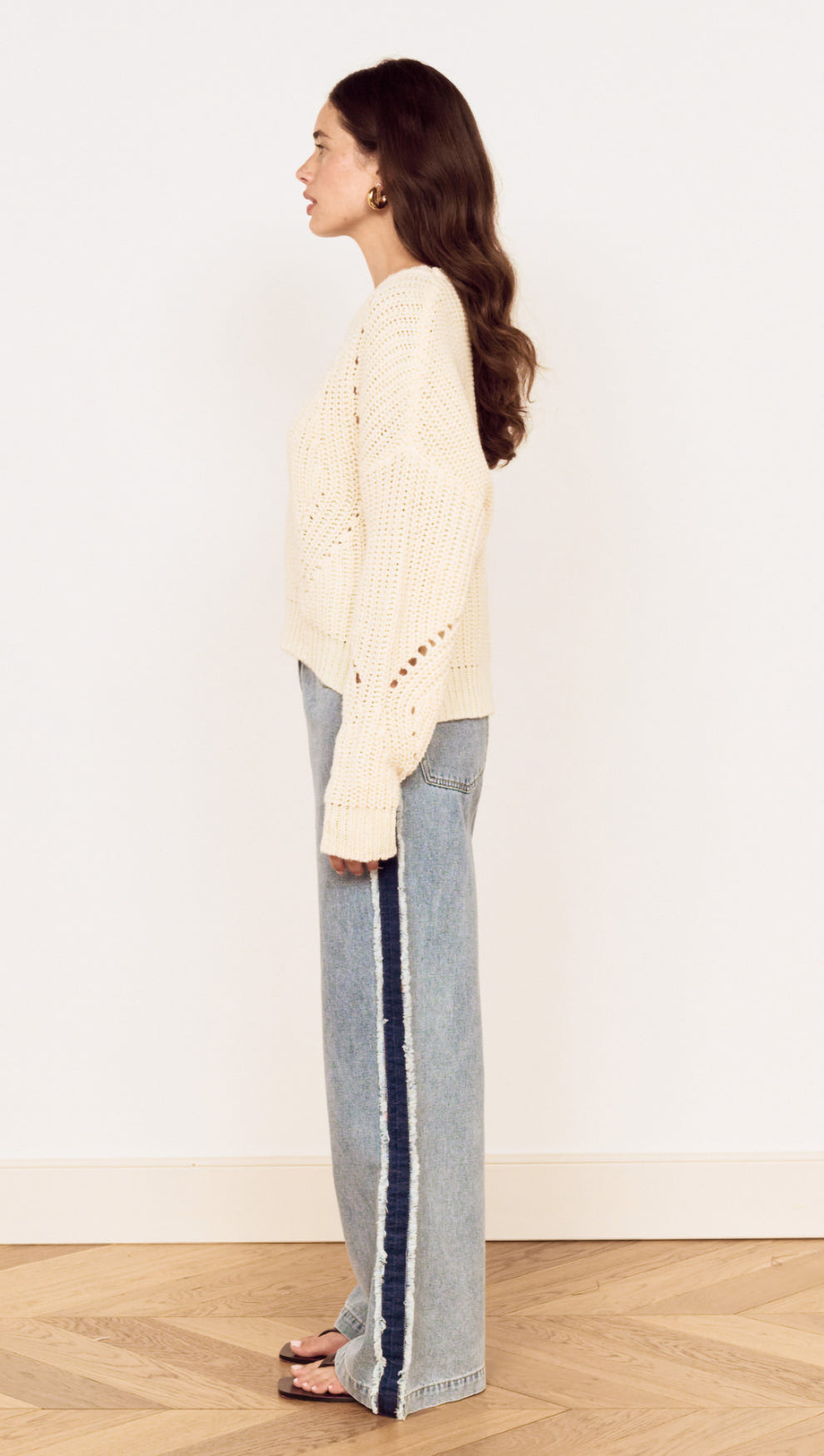 Side view of a model wearing a Cream Round Neck Open Knit Jumper with relaxed fit denim for a casual look.