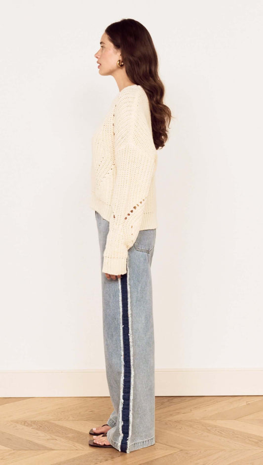 Side view of a model wearing a Cream Round Neck Open Knit Jumper with relaxed fit denim for a casual look.