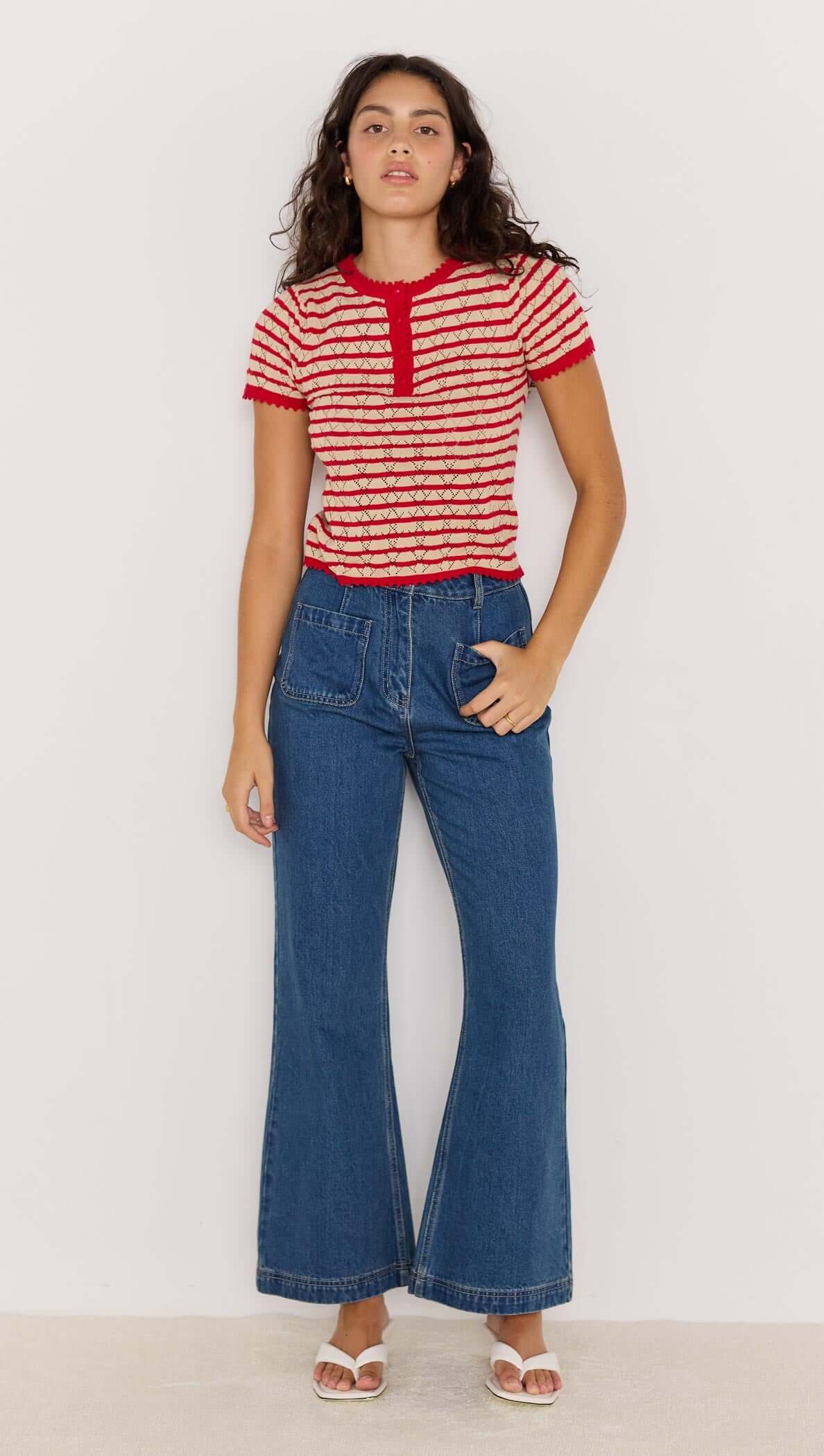Model wearing CHLOE STRIPE KNIT TEE in red with beige stripes, paired with flared blue jeans and sandals.