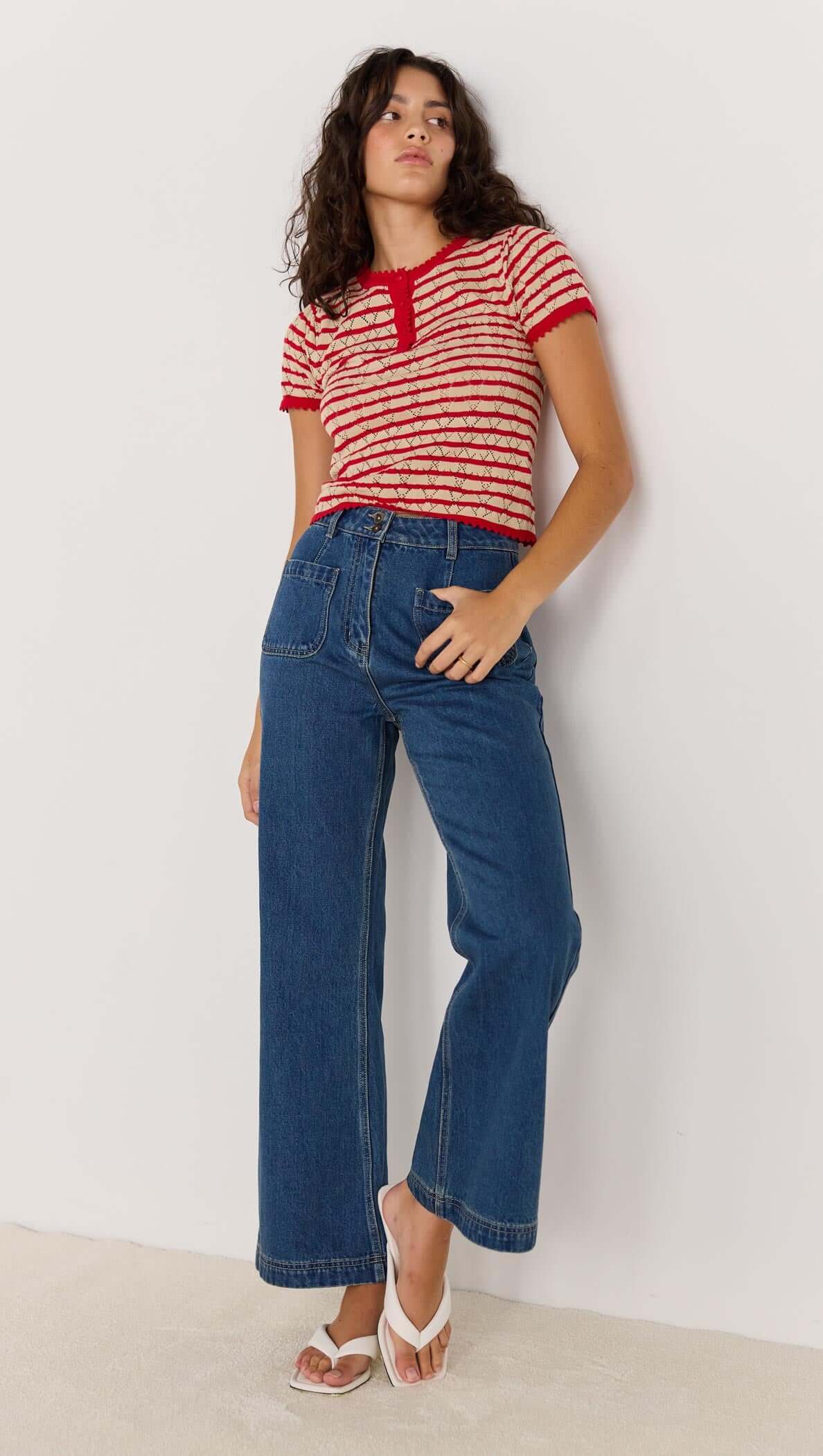 Chloe Stripe Knit Tee in red and beige stripes, featuring short sleeves and a Henley-style neckline, styled with wide-leg jeans.