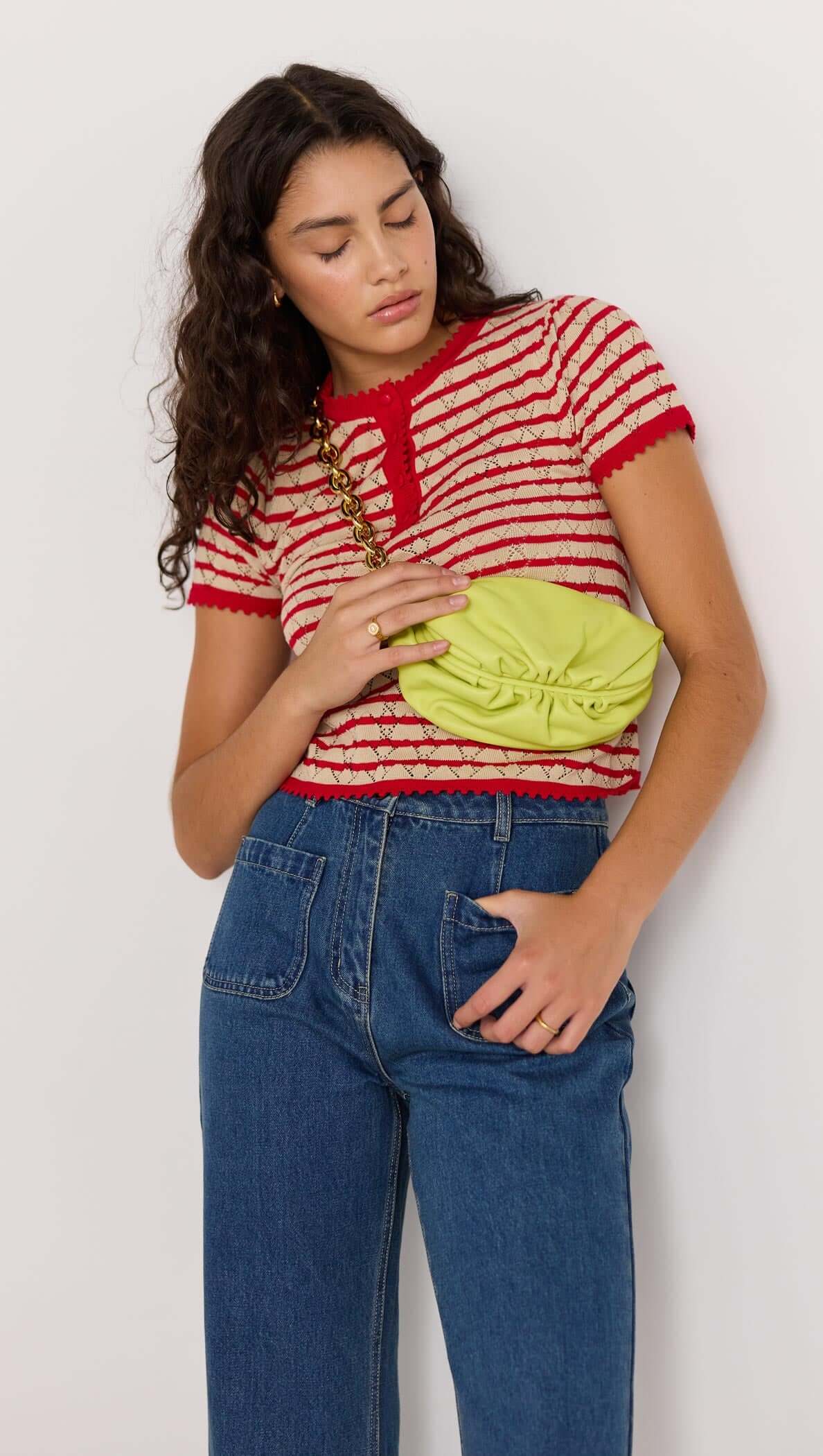 Woman wearing a CHLOE STRIPE KNIT TEE with red and beige stripes, holding a green bag.
