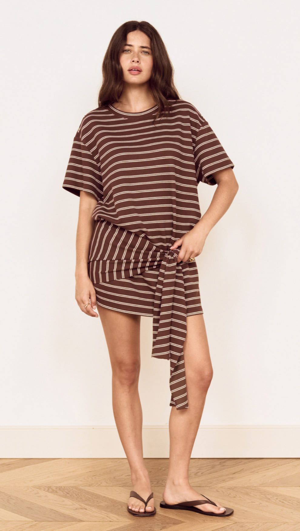 Model wearing Striped Tie Waist Jersey Mini Dress with chocolate stripes and an adjustable tie at the waist.