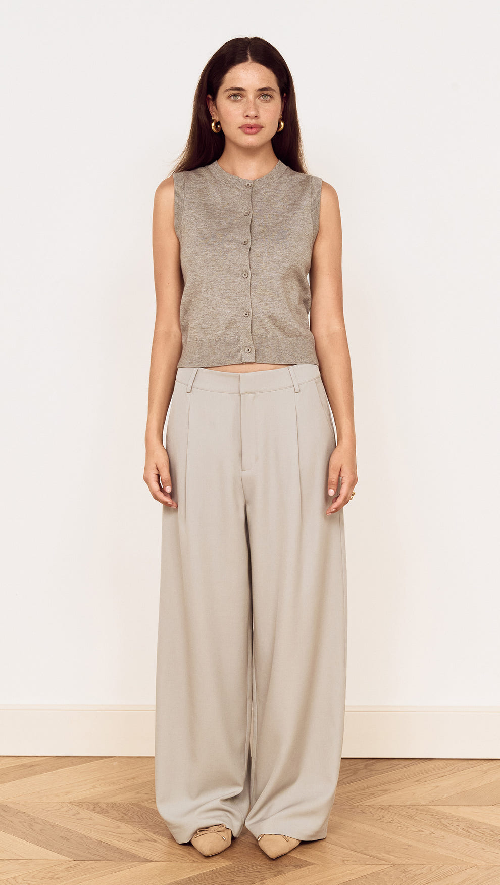 Model wearing a Round Neck Knitted Vest in Soft Grey with high-waisted light grey trousers, showcasing a minimalist style.