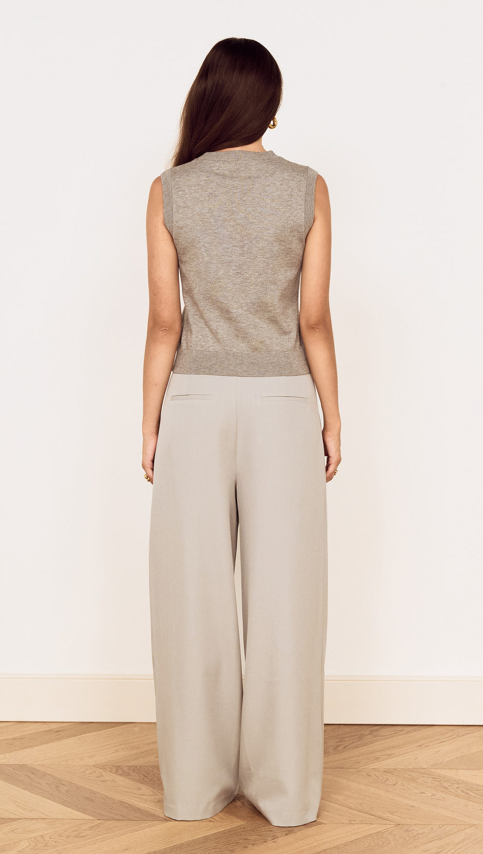 Model wearing the Round Neck Knitted Vest in Soft Grey, showcasing the back view with wide-leg trousers.