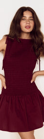 Model wearing a Cotton Shirred Mini Dress in Burgundy with a shirred bodice and gathered skirt, showcasing a feminine silhouette.