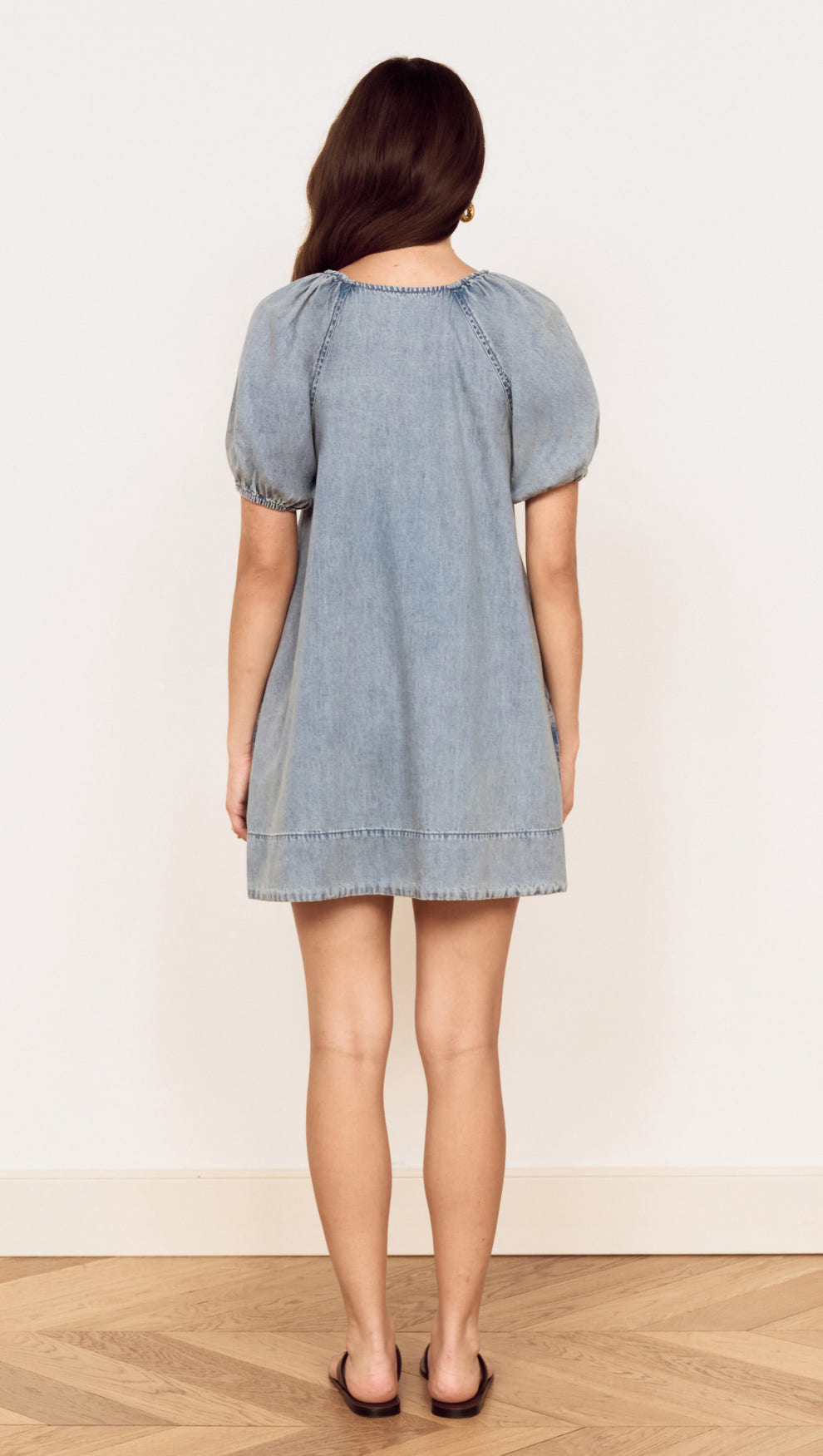 Back view of a woman wearing the Puff Sleeve Fluid Denim Mini Dress in soft washed denim.
