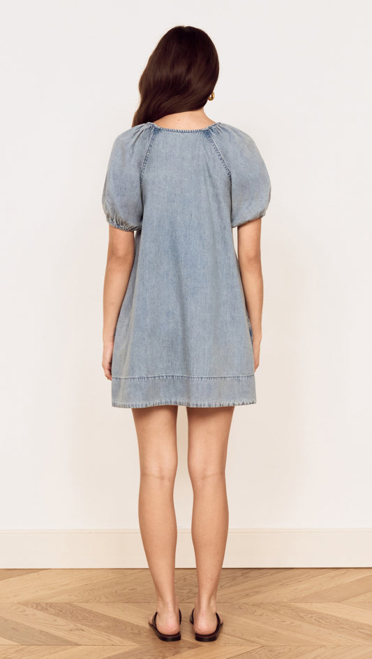 Back view of a woman wearing the Puff Sleeve Fluid Denim Mini Dress in soft washed denim.