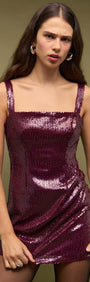 Model wearing a Purple Sequin Mini Dress with a square neckline and wide straps, showcasing a shimmering burgundy design.