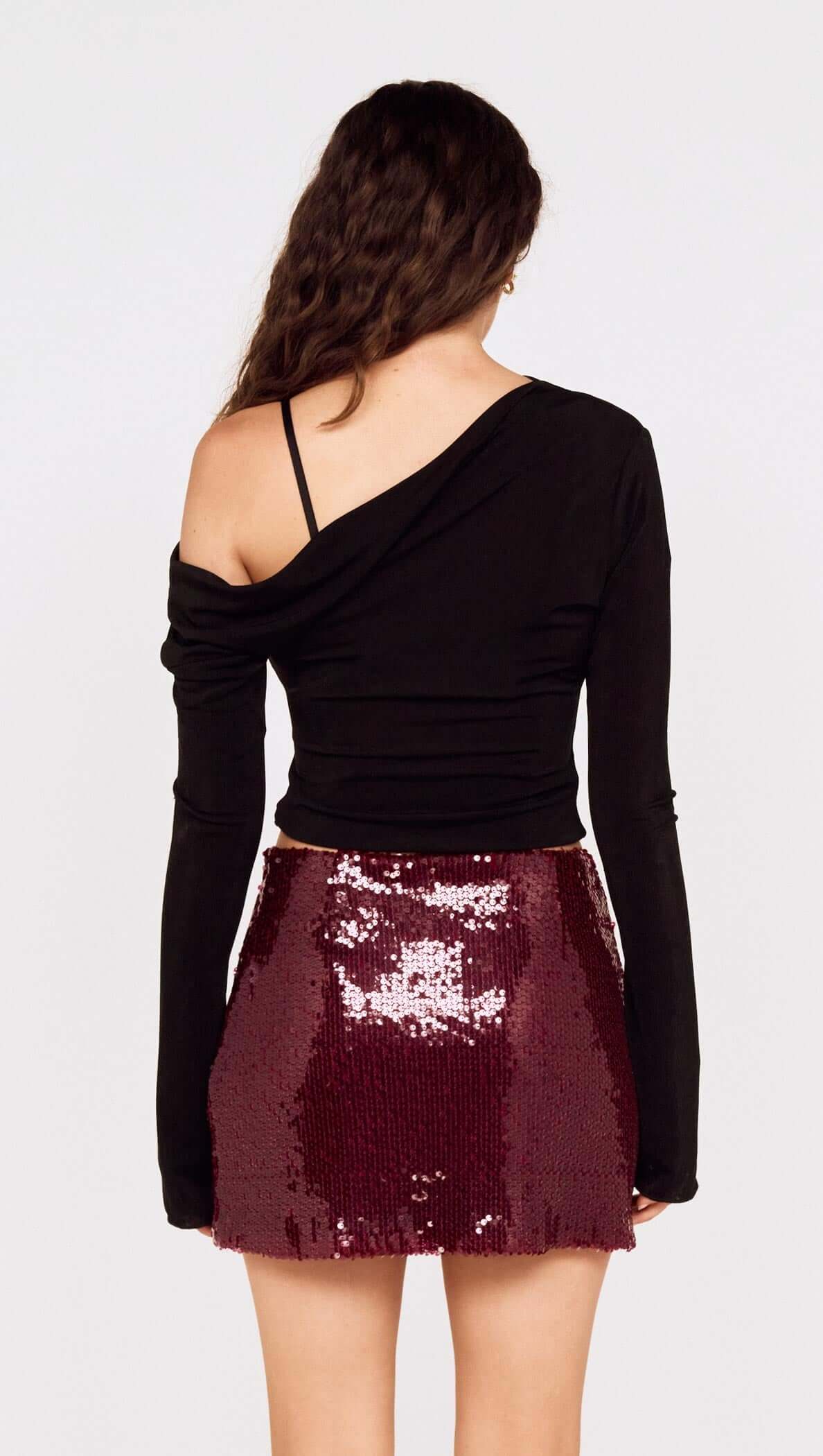 Model wearing a fitted black top with the Purple Sequin Mini Skirt, showcasing its sparkling deep burgundy sequins.