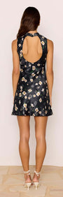Back view of a model wearing the Elinor Black Floral Bias Mini Dress with an open back and floral print.