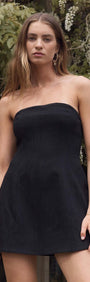 Model wearing a Black Strapless Peplum Mini Dress posed outdoors among greenery.