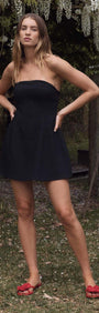 Model wearing a Black Strapless Peplum Mini Dress in an outdoor setting with greenery.