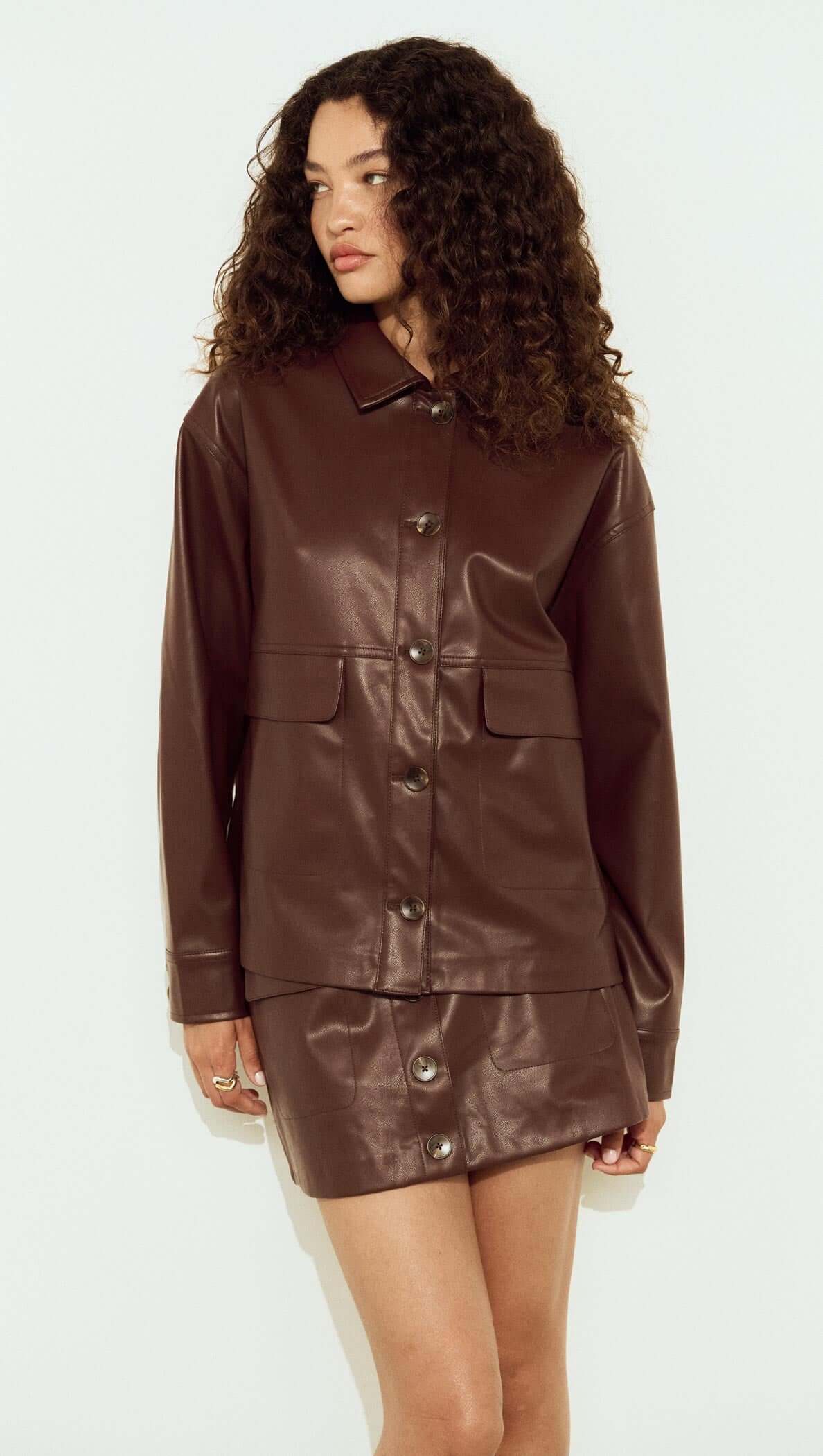 Model wearing a Brown Faux Leather Jacket styled with a matching skirt, showcasing a relaxed silhouette and button-front design.